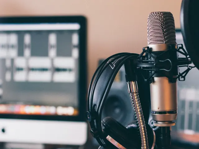 Micrófono de estudio junto a auriculares y una pantalla con software de audio